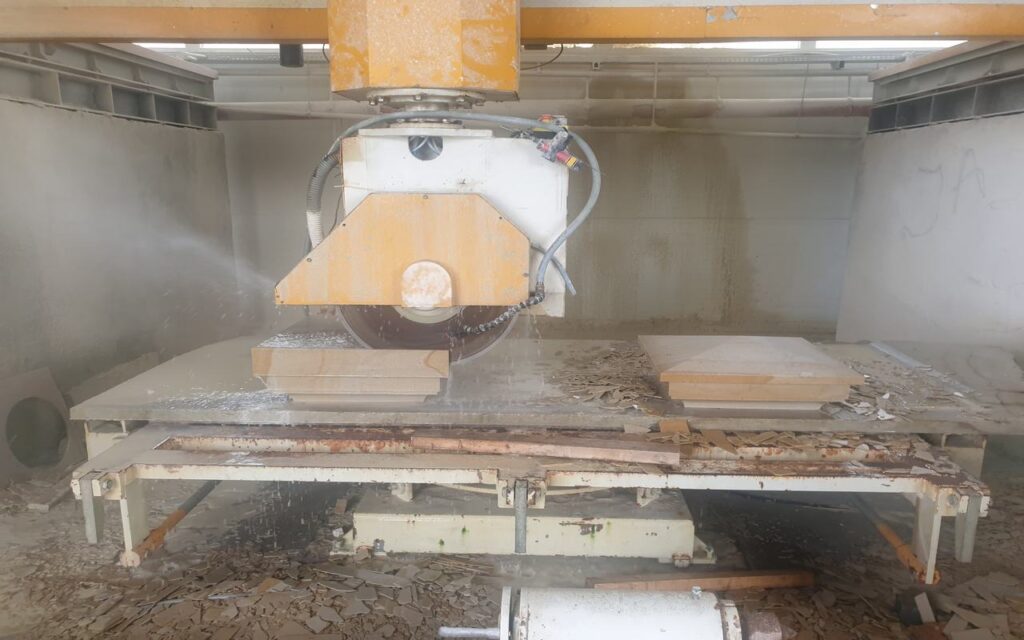 Obróbka piaskowca przy użyciu wielkoformatowej piły diamentowej. Maszyna precyzyjnie tnie kamień, tworząc gładkie i równe powierzchnie, idealne do dalszej obróbki lub bezpośredniego montażu. Woda widoczna podczas cięcia służy do chłodzenia ostrza oraz redukcji pylenia, co zwiększa efektywność i bezpieczeństwo procesu.